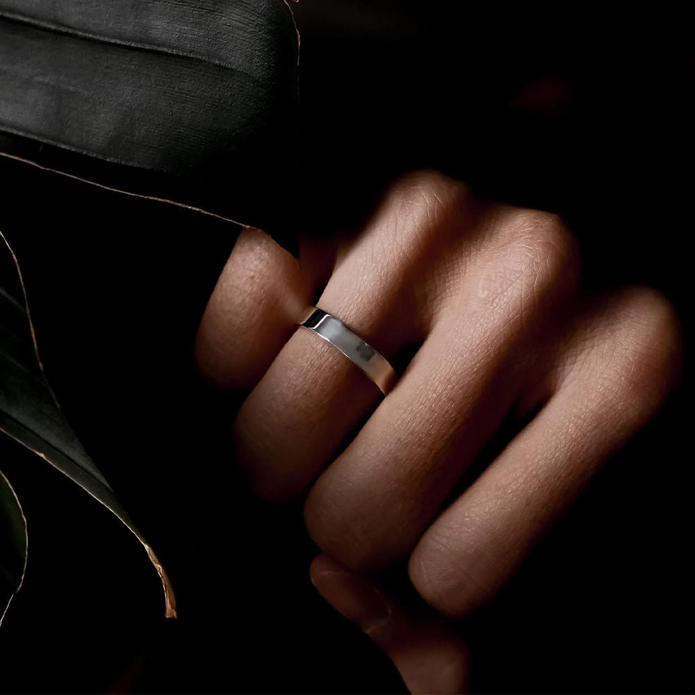 Silver ring on a person's finger with a dark background