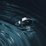 Silver ring with a unique design submerged in water, creating ripples.