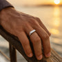 Hand wearing a silver ring with a blurred sunset background