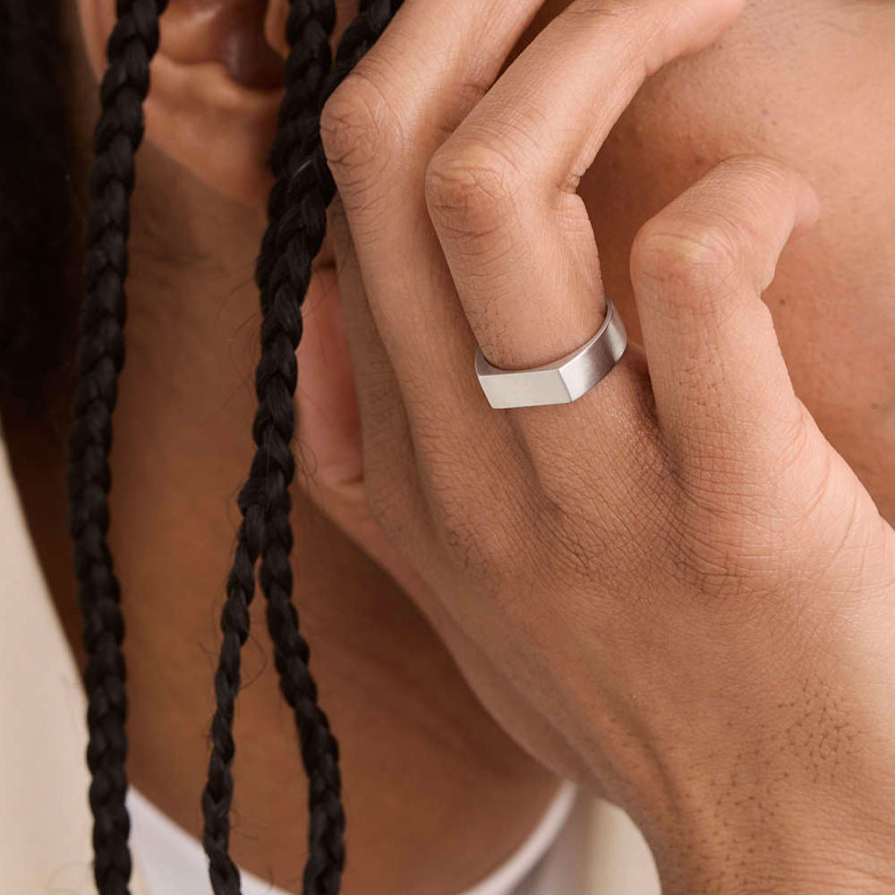 Hand wearing a silver ring with braided hair in the background