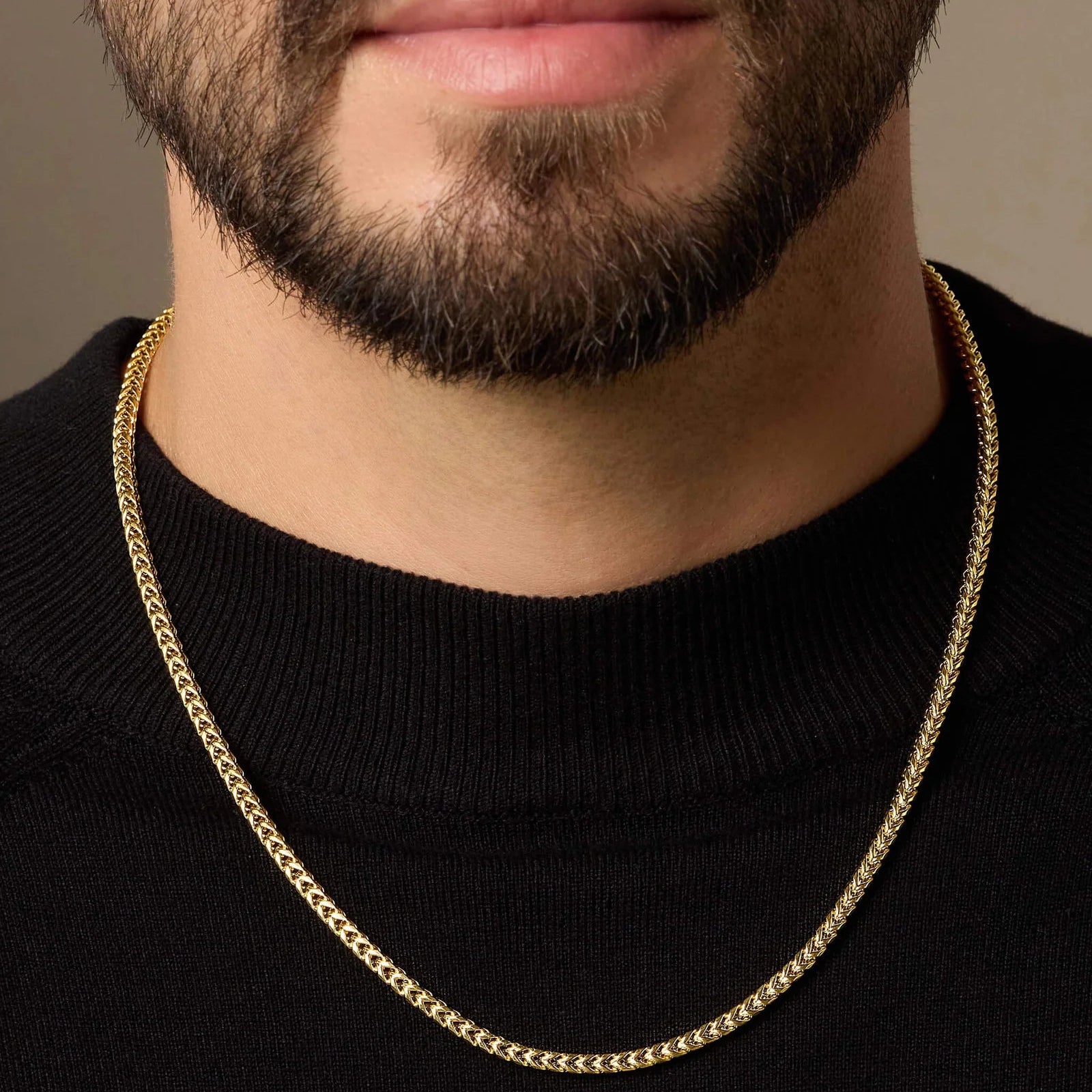 Gold chain necklace worn by a person with a neutral background