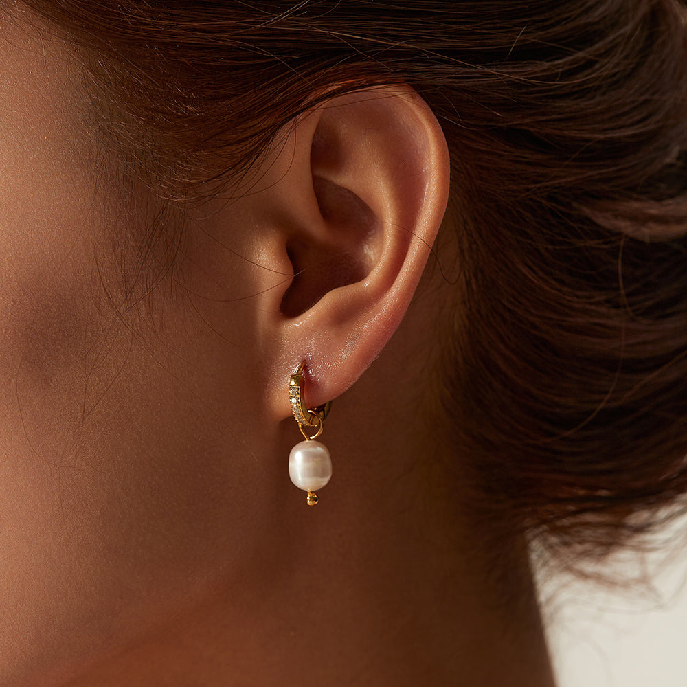 Close-up of an ear wearing a gold earring with a pearl drop.