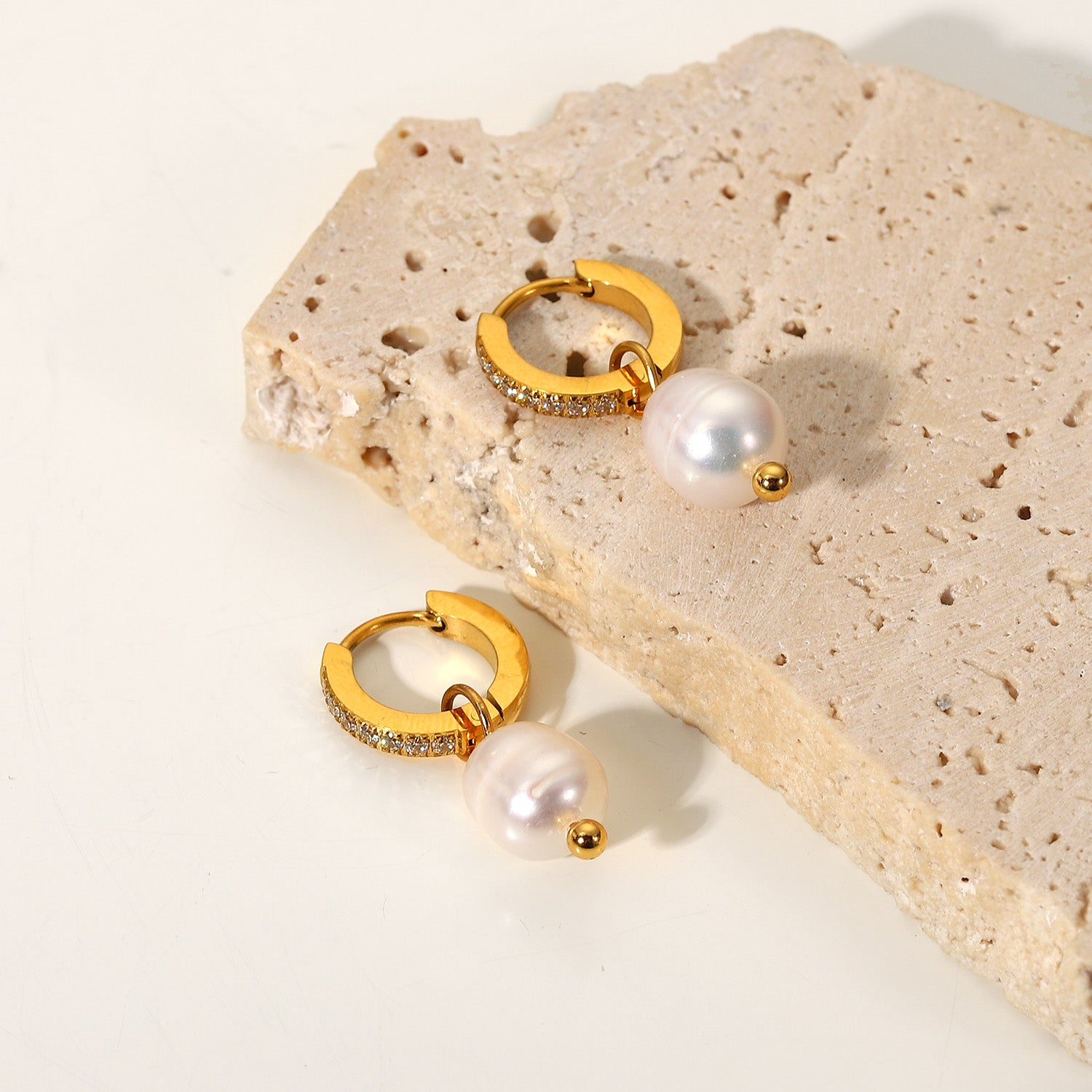 Gold hoop earrings with pearls on a textured beige surface
