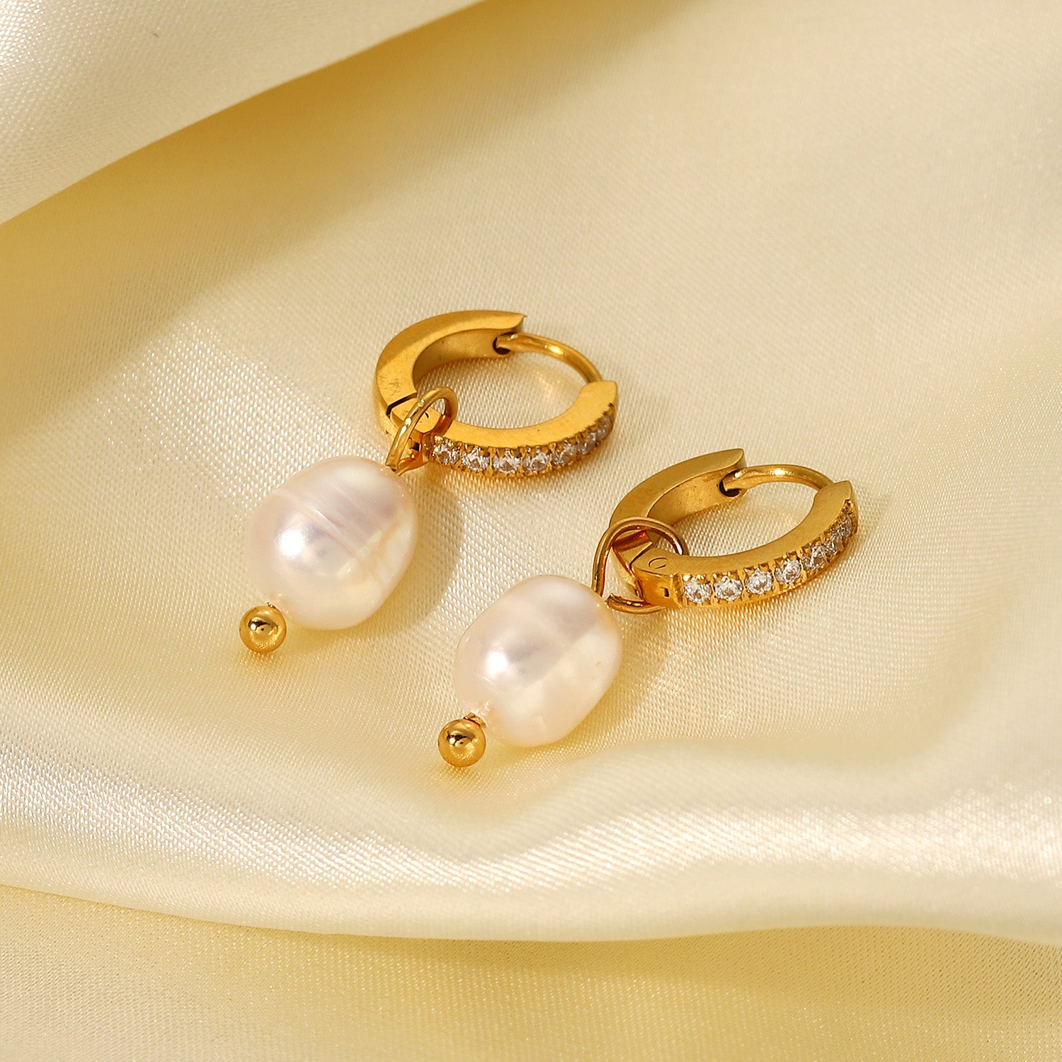 Gold hoop earrings with pearl and gemstone accents on a beige fabric background