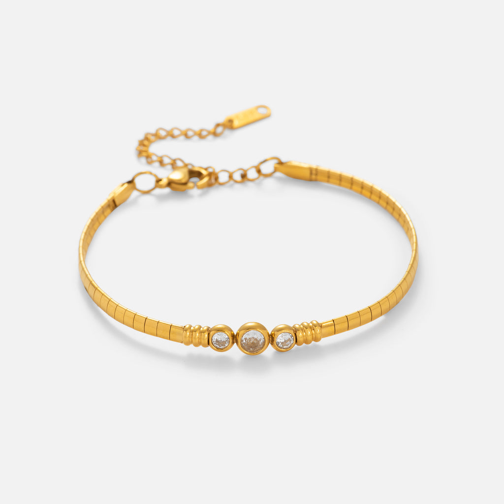 Gold bracelet with three circular charms on a light beige background