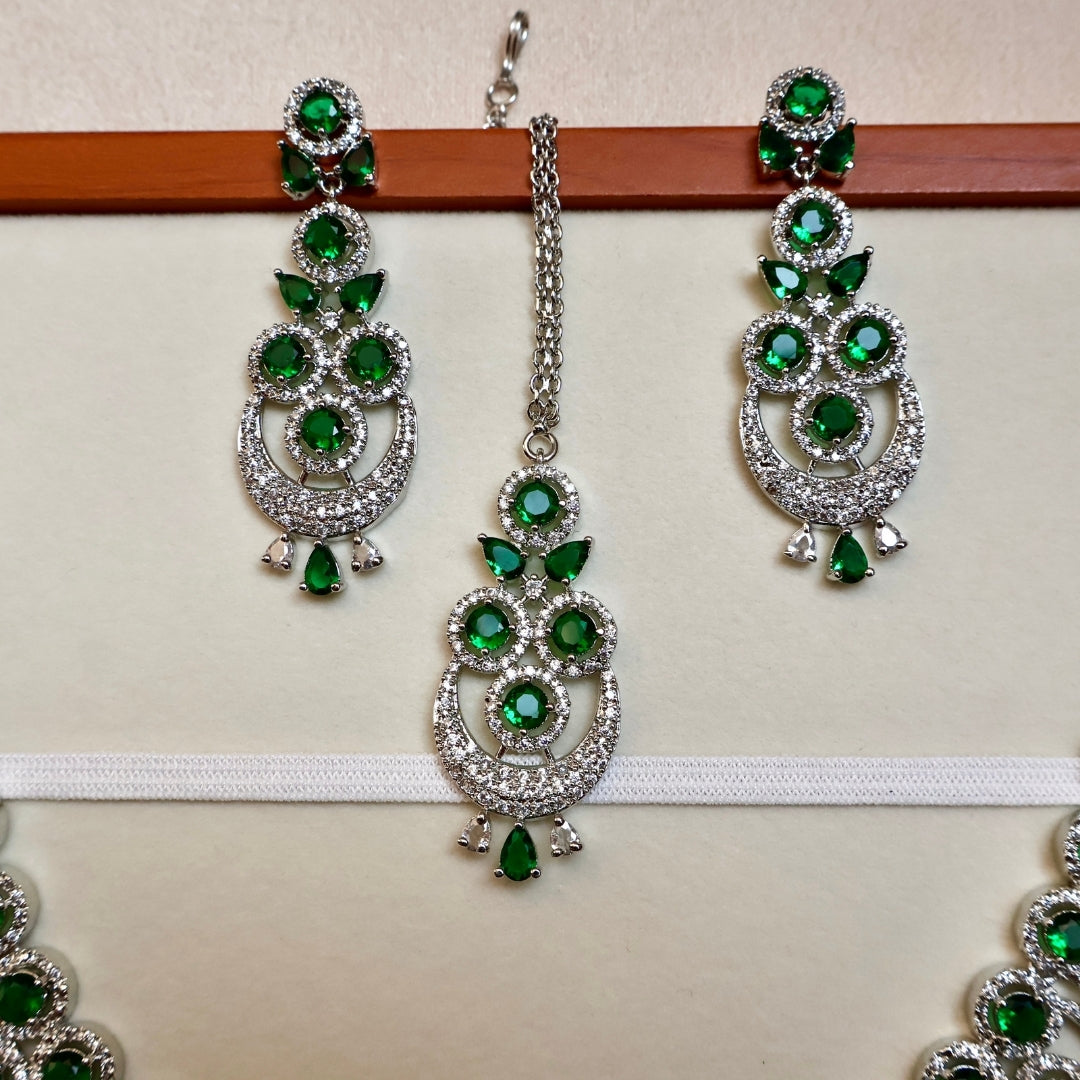 Green and silver earrings on a wooden stick against a beige background