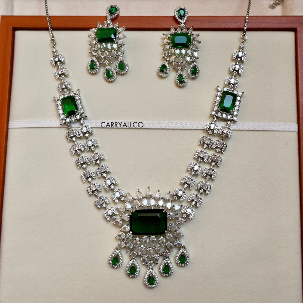 Jewelry set with necklace and earrings featuring green gemstones on a beige background.