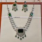 Jewelry set with necklace and earrings featuring green gemstones on a beige background.