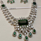 Jewelry set with necklace and earrings featuring green gemstones and clear stones on a light background.