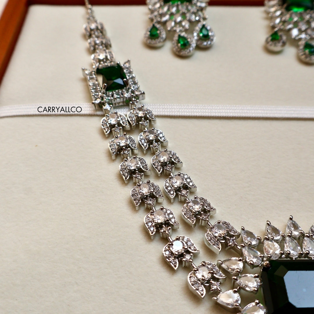 Silver necklace with green gemstones on a beige background, brand 'CARRYALICO' visible.