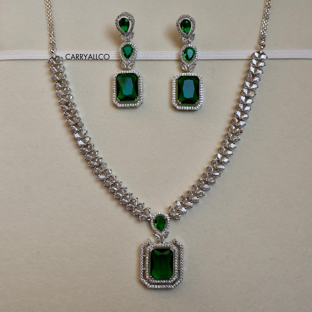Jewelry set with necklace and earrings featuring green gemstones on a beige background.