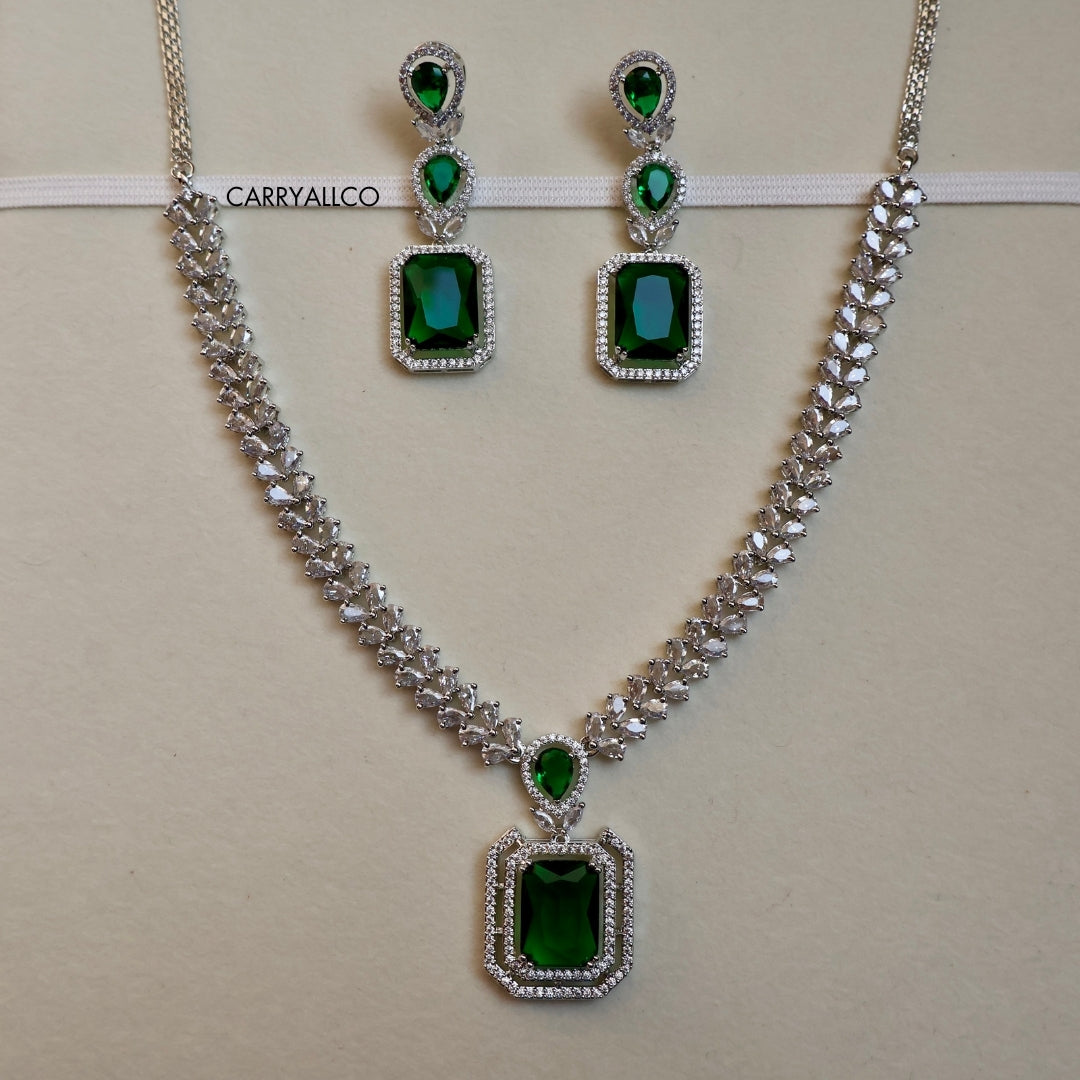 Jewelry set with necklace and earrings featuring green gemstones on a beige background.