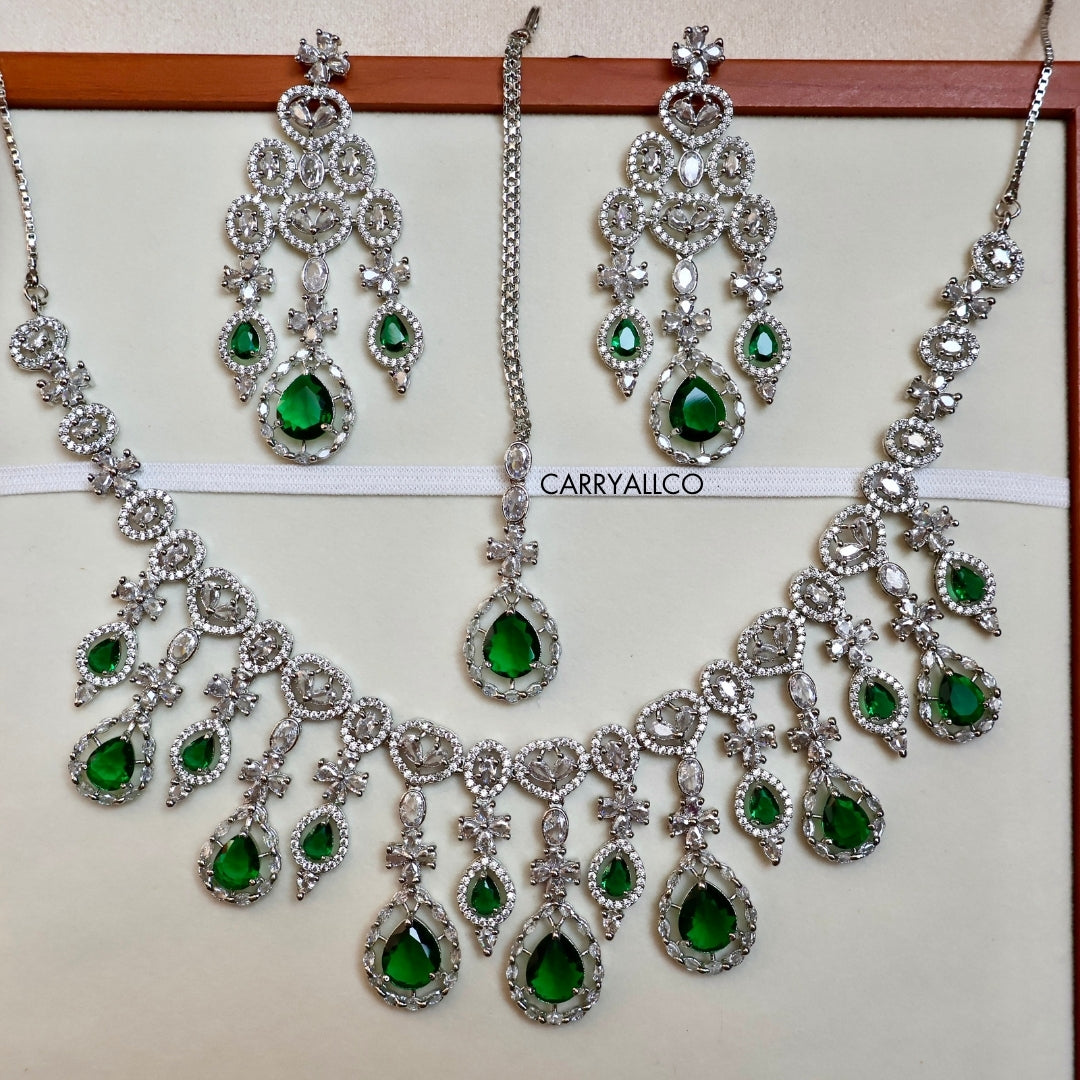 Jewelry set with necklaces and earrings featuring green gemstones on a white background.