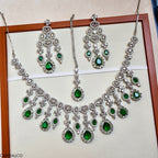 Jewelry set with necklace and earrings featuring green gemstones on a beige background.