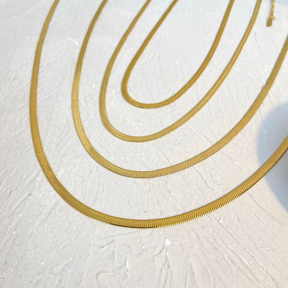 Gold necklaces of different lengths on a textured white surface