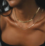 A close-up of a model wearing a double-layered gold chain necklace, featuring a thin wavy chain and a slightly thicker bolder chain.