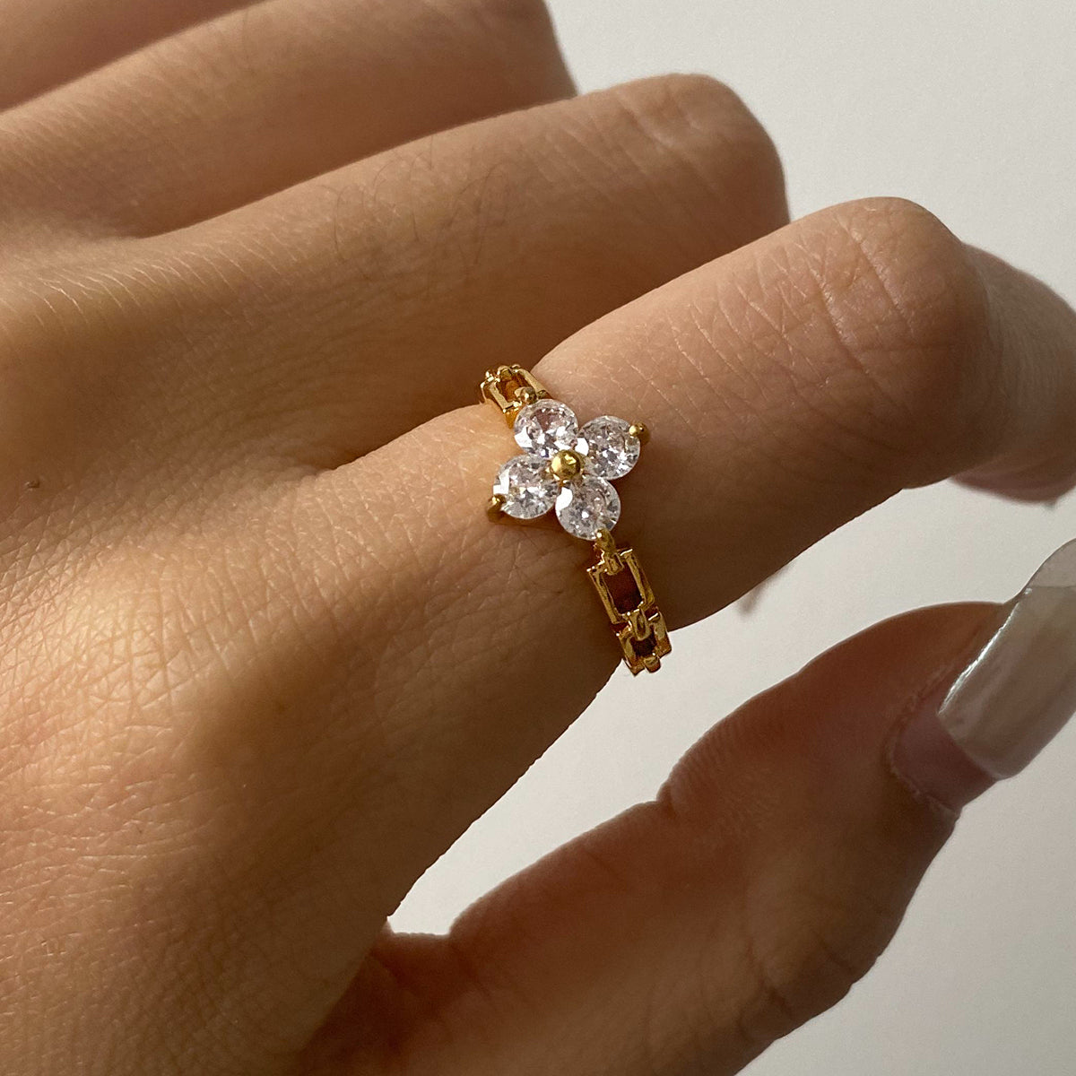 Gold ring with a floral design on a person's finger against a neutral background