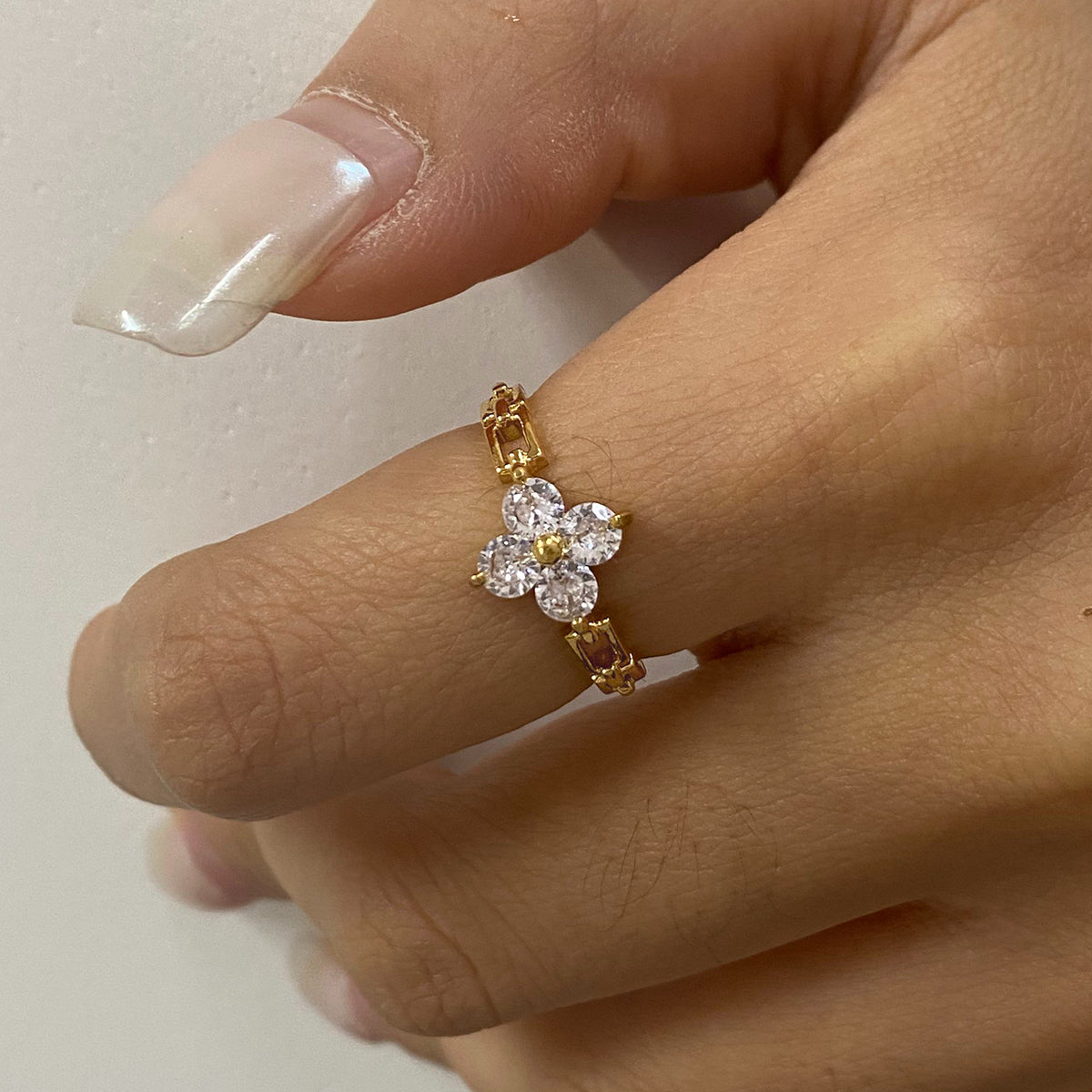 Gold flower-shaped ring with diamonds on a finger against a neutral background