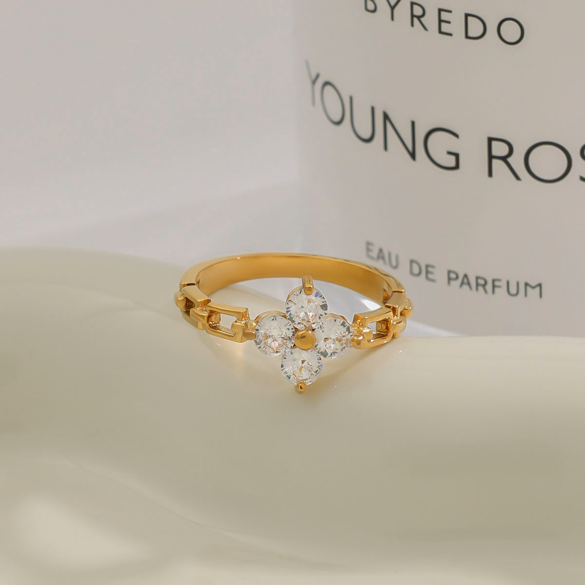 Gold ring with floral design on a Byredo Young Rose perfume bottle background