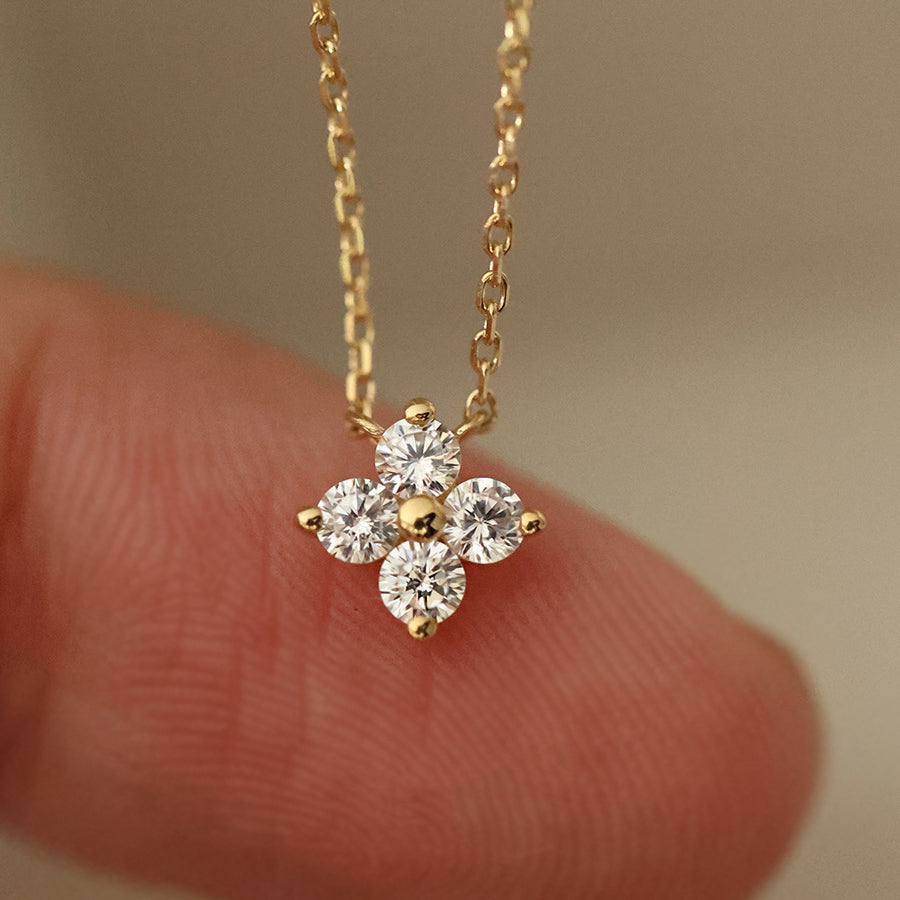 Gold necklace with a diamond pendant held between fingers against a neutral background