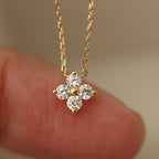 Gold necklace with a diamond pendant held between fingers against a neutral background