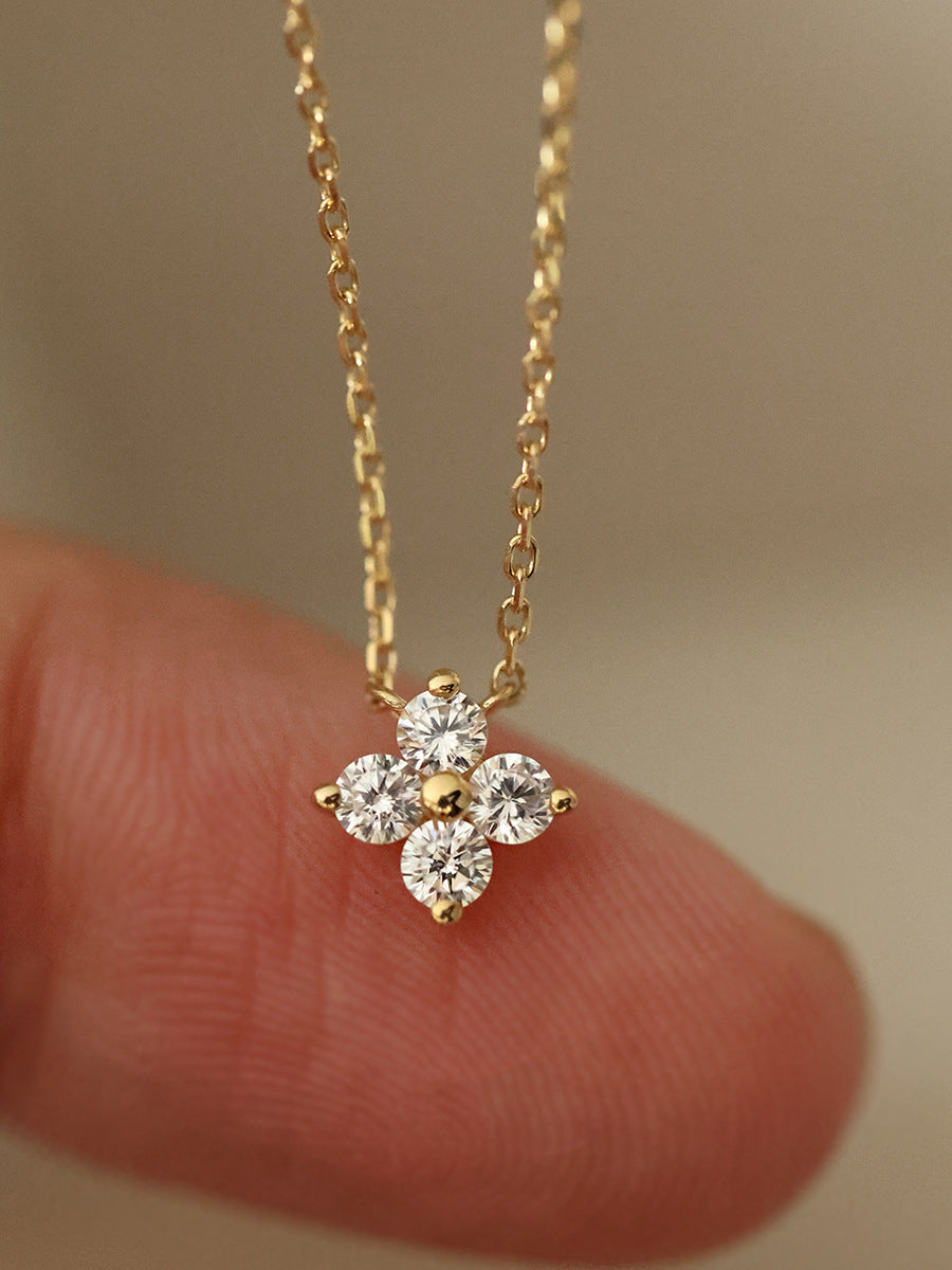 Gold necklace with a diamond pendant held between fingers against a neutral background