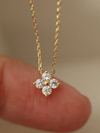 Gold necklace with a diamond pendant held between fingers against a neutral background