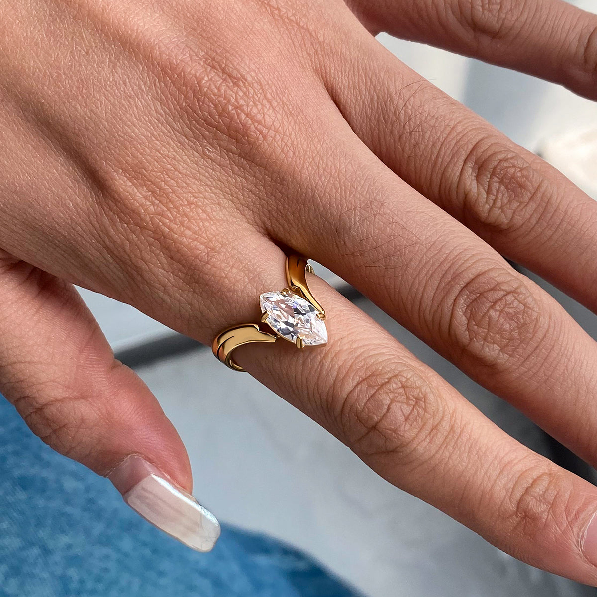 Gold ring with a large diamond on a person's finger against a blurred background