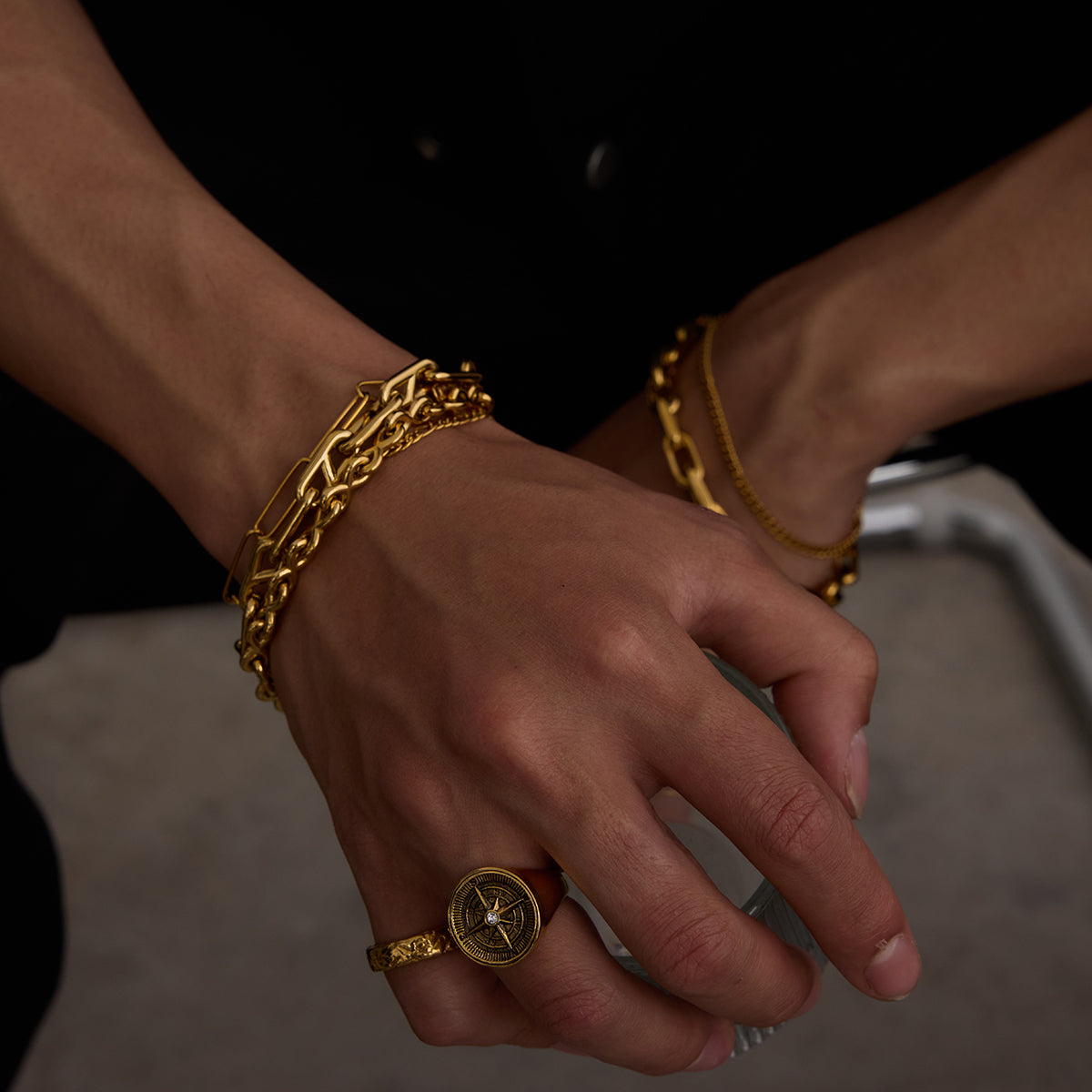 Close-up of a hand wearing gold bracelets and a ring on a dark background