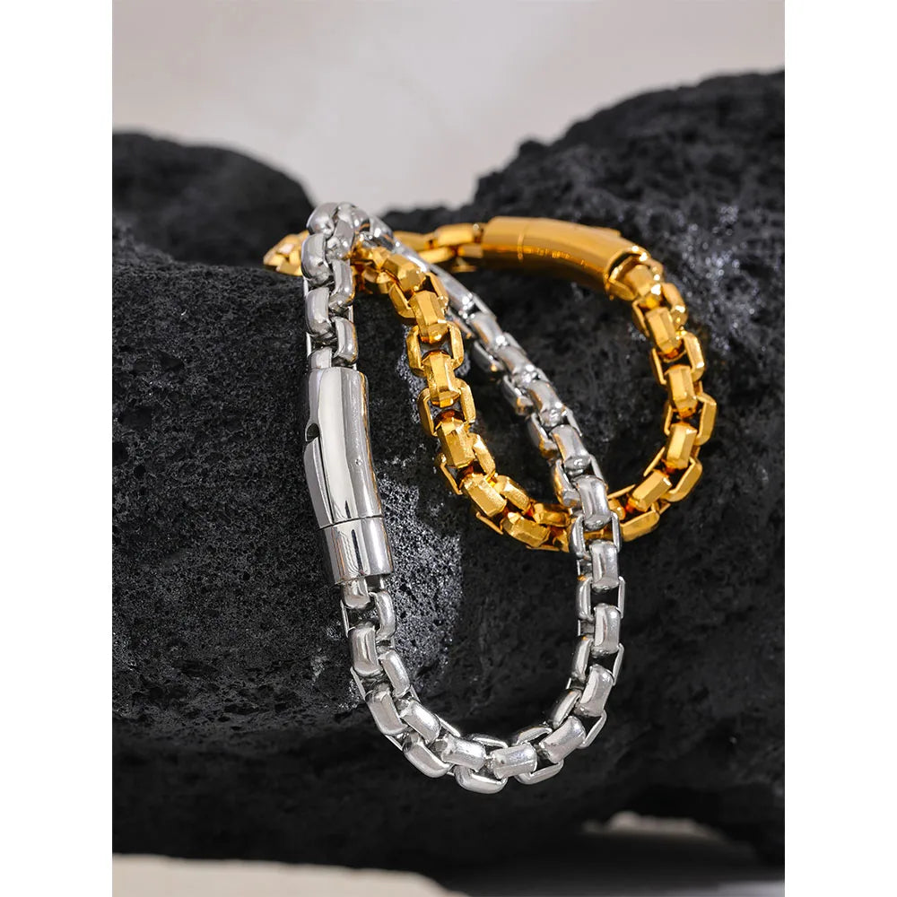 Two bracelets, one gold and one silver, on a textured black surface.