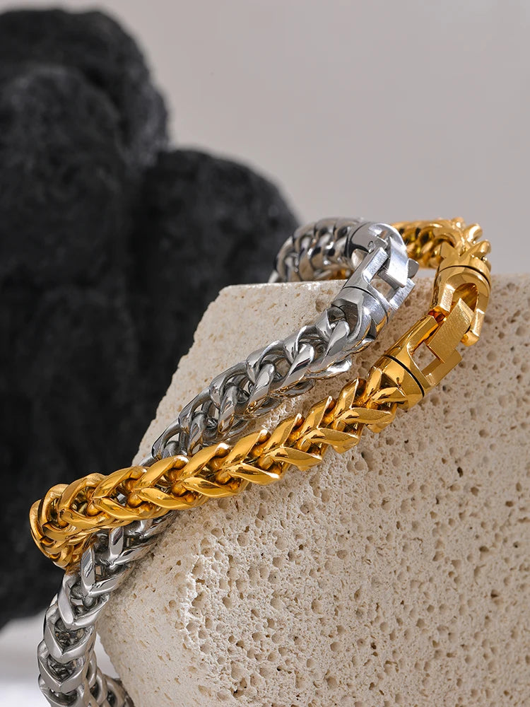 Two gold and silver chain bracelets on a textured stone surface.