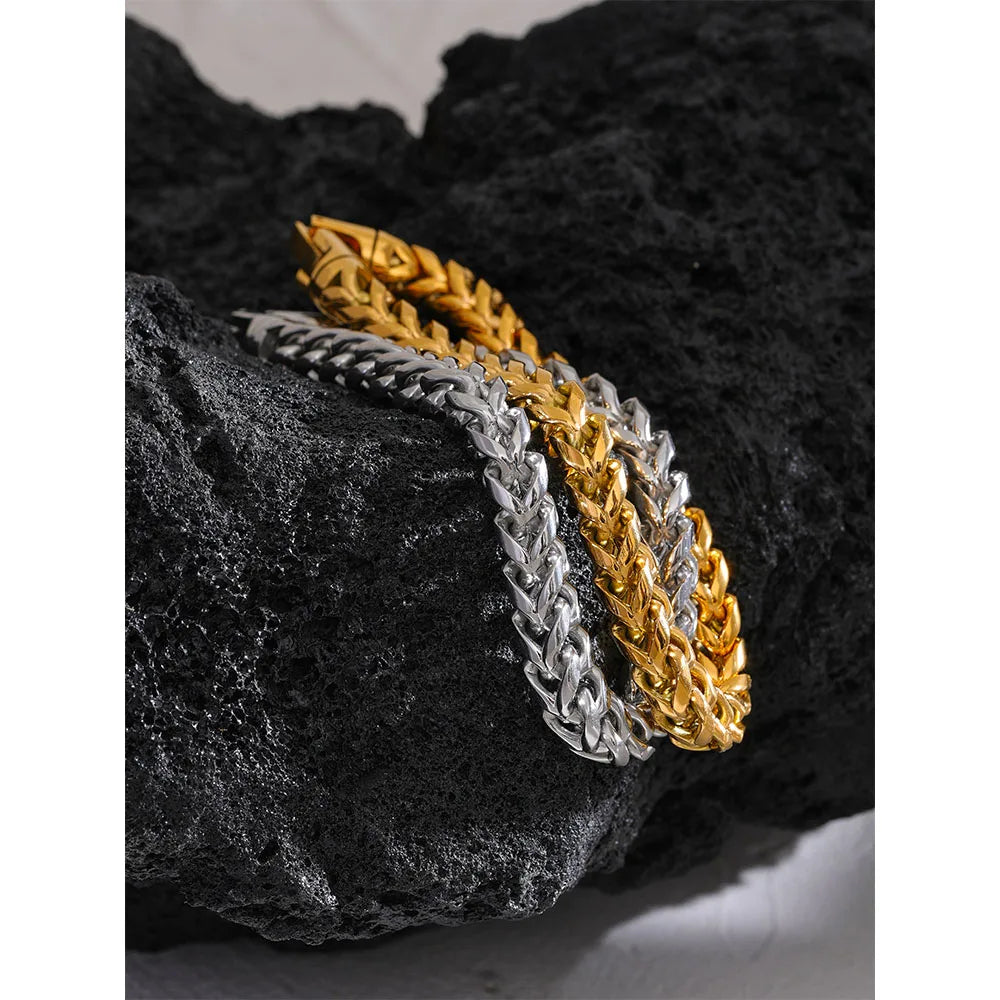 Two braided bracelets, one gold and one silver, on a textured black surface.