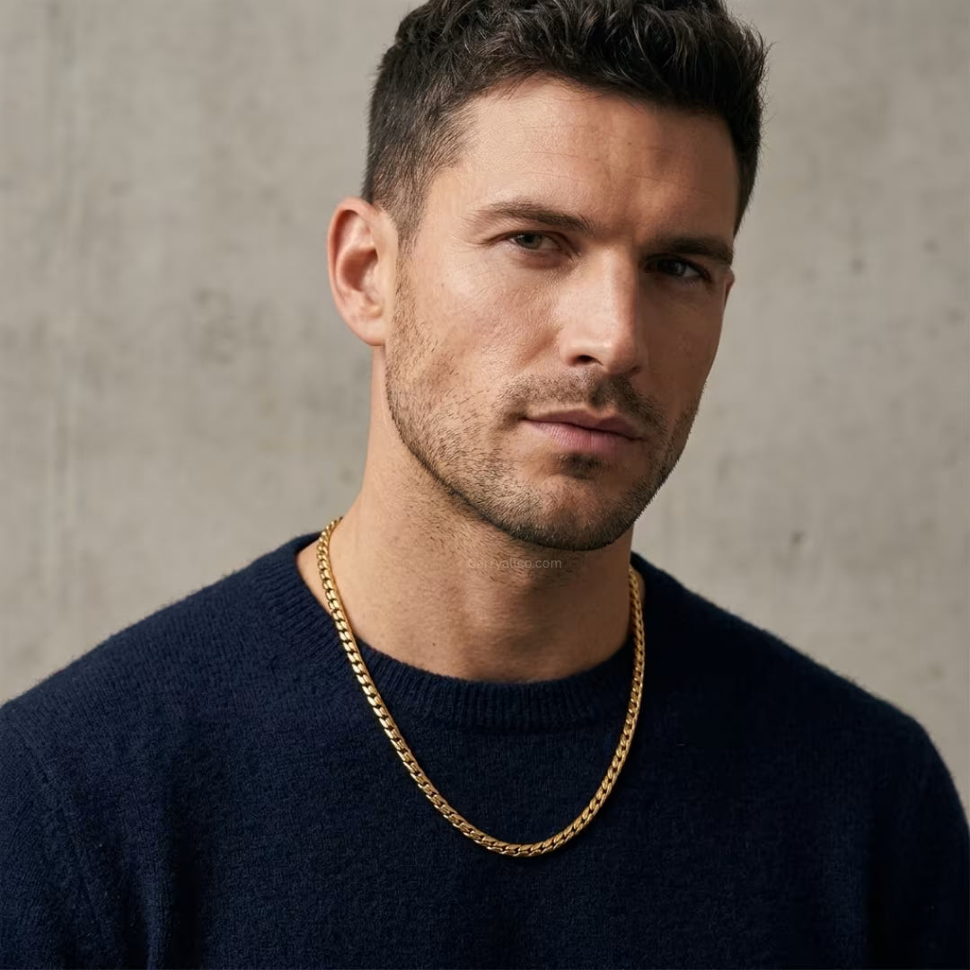 Man wearing a dark sweater and gold chain necklace against a neutral background