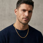 Man wearing a dark sweater and gold chain necklace against a neutral background