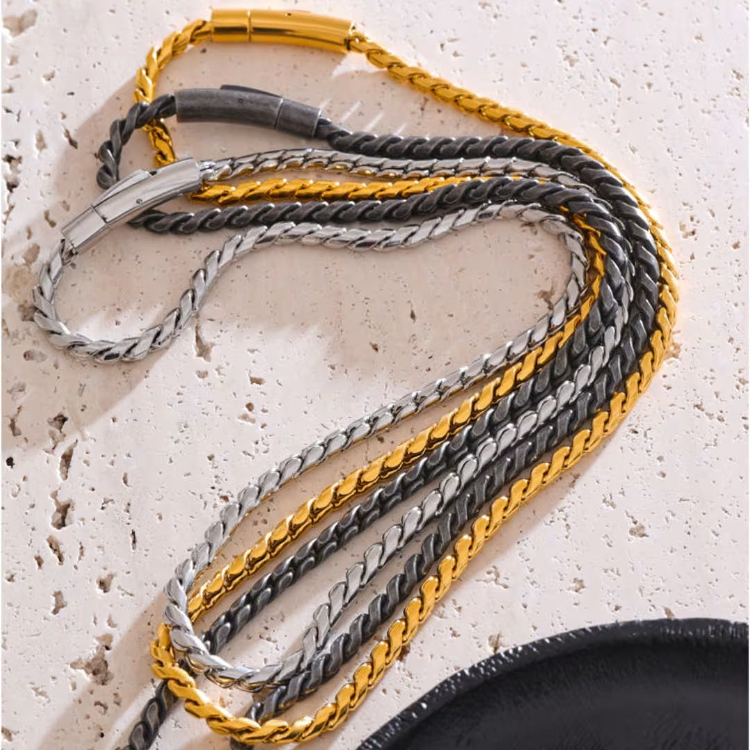 Three braided leather straps in gold, silver, and black on a textured surface.