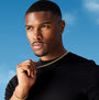 Man wearing a black shirt and gold jewelry against a blue sky