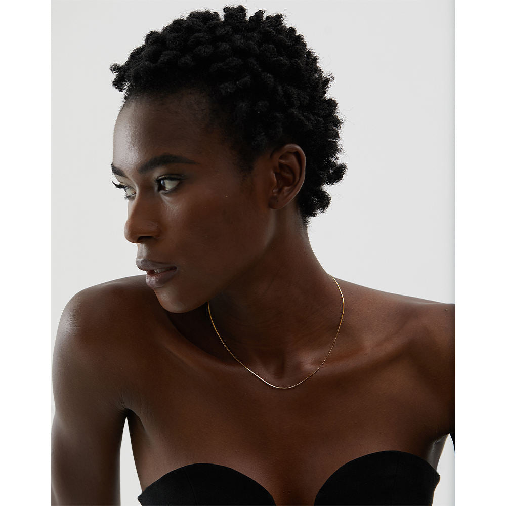 Woman wearing a gold necklace against a neutral background