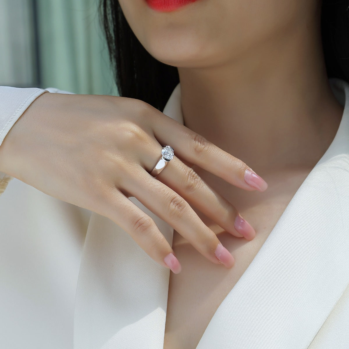 Close-up of a hand wearing a silver ring with a diamond, against a neutral background.