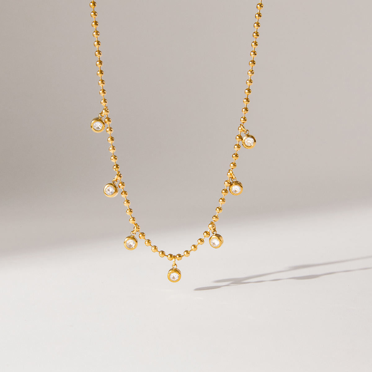 Gold necklace with small pearls on a light gray background