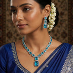Woman wearing a blue saree with matching jewelry against a patterned background
