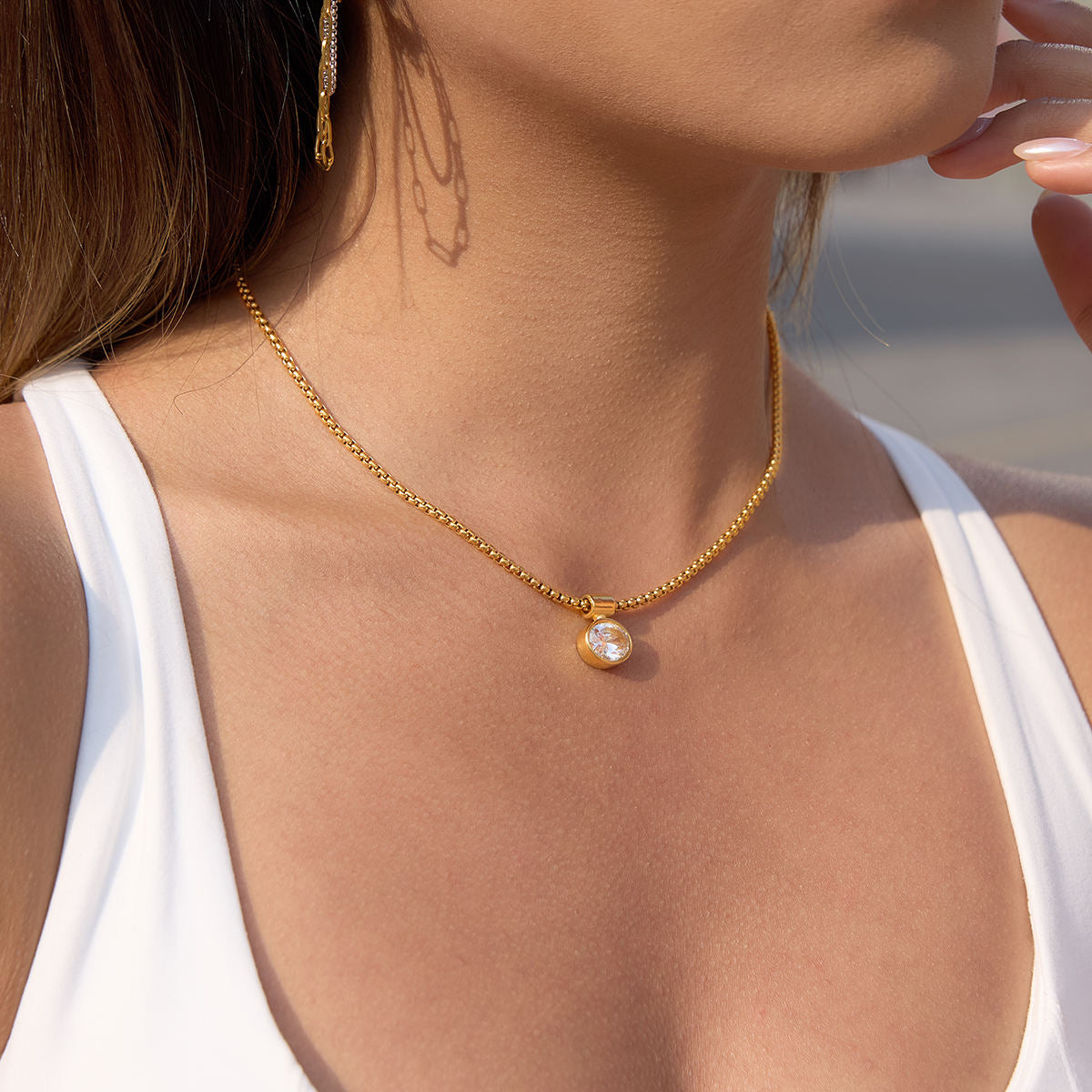 Close-up of a person wearing a gold necklace with a pendant.