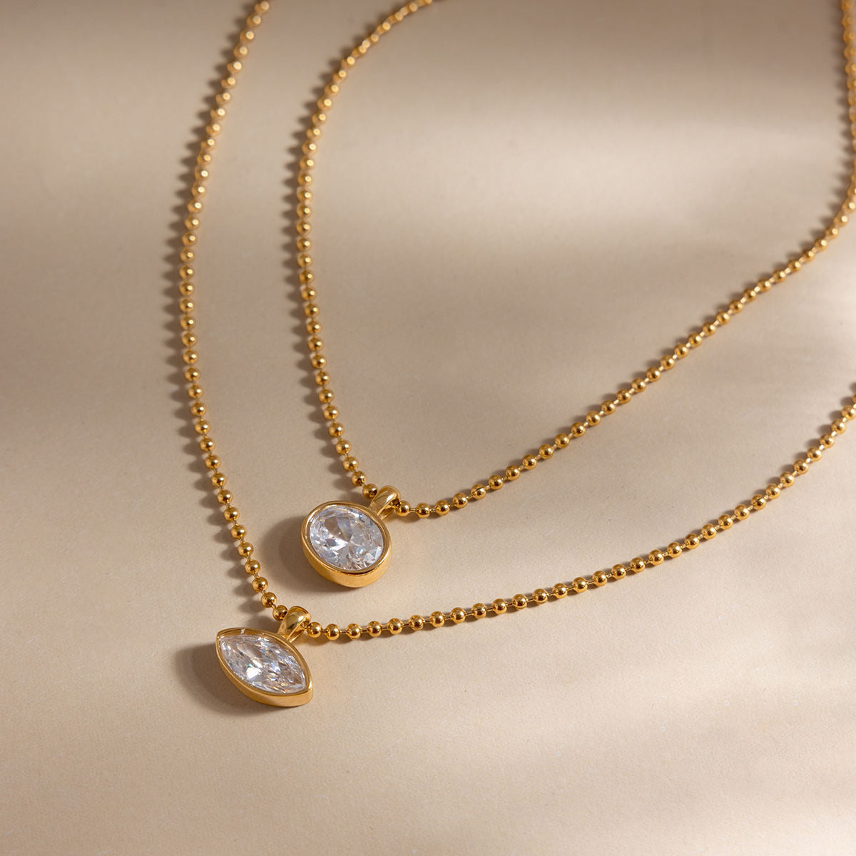 Gold necklaces with teardrop-shaped crystals on a beige background