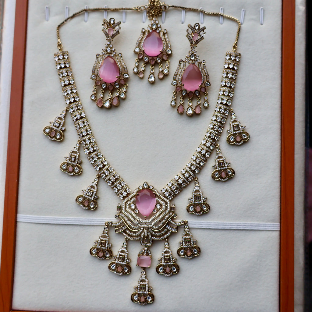 Ornate necklace and earrings set with pink stones on a white background