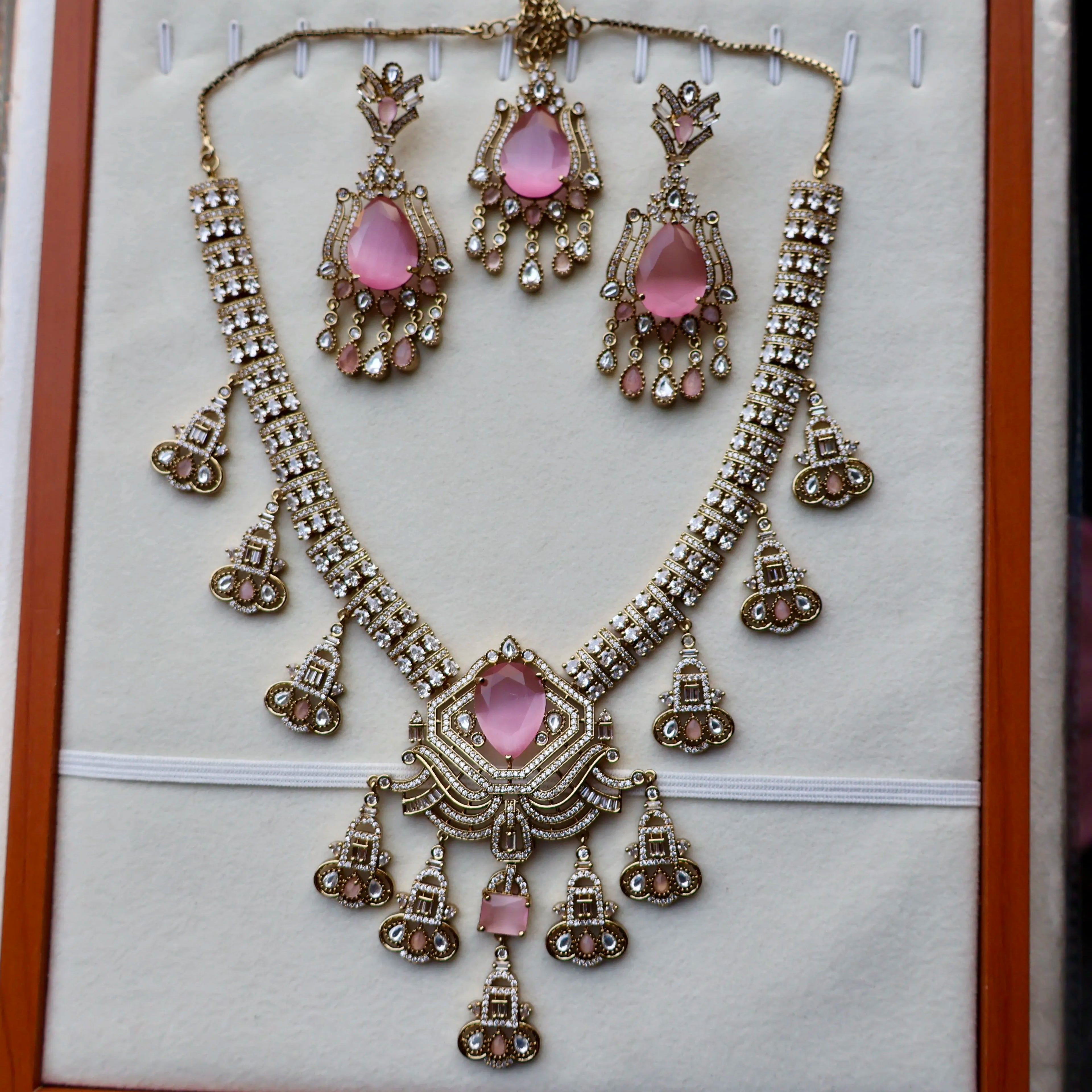 Ornate necklace and earrings set with pink stones on a white background