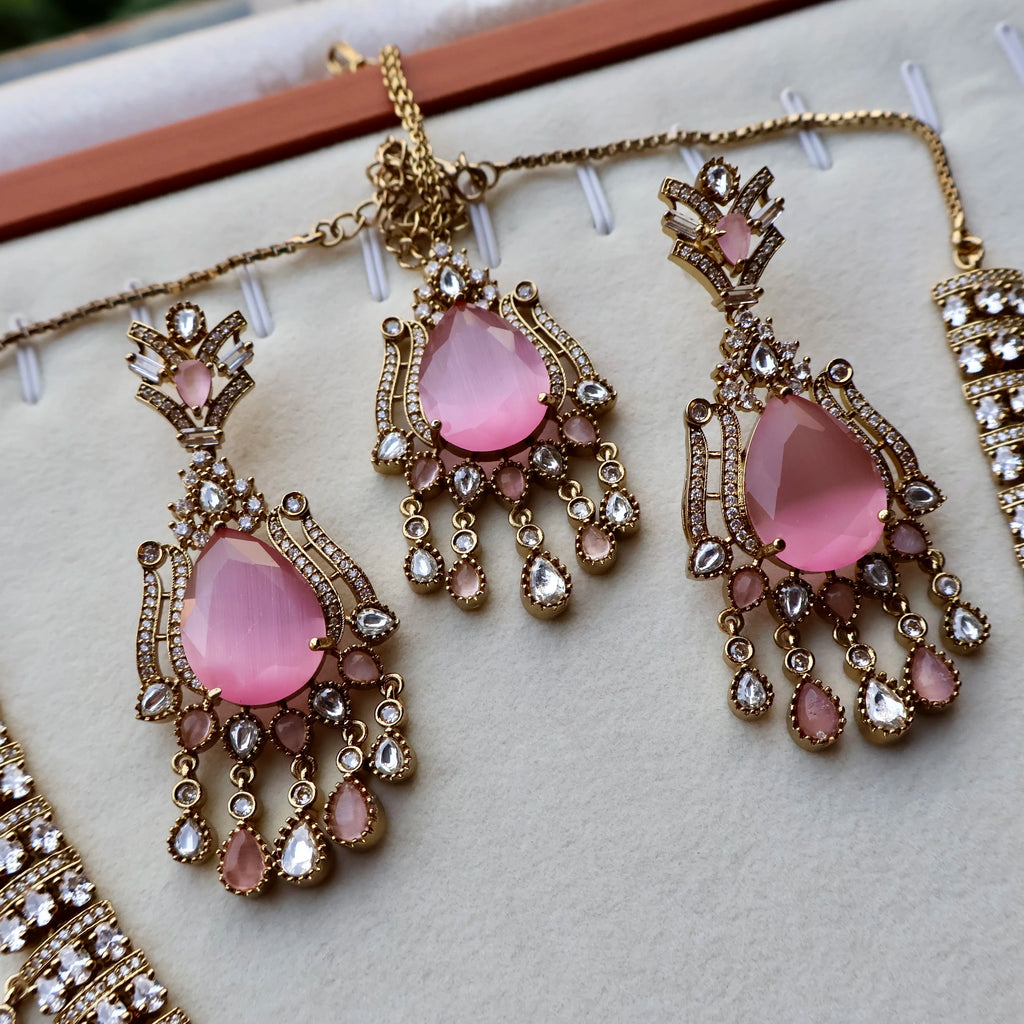Pink teardrop earrings with gold and crystal details on a white surface