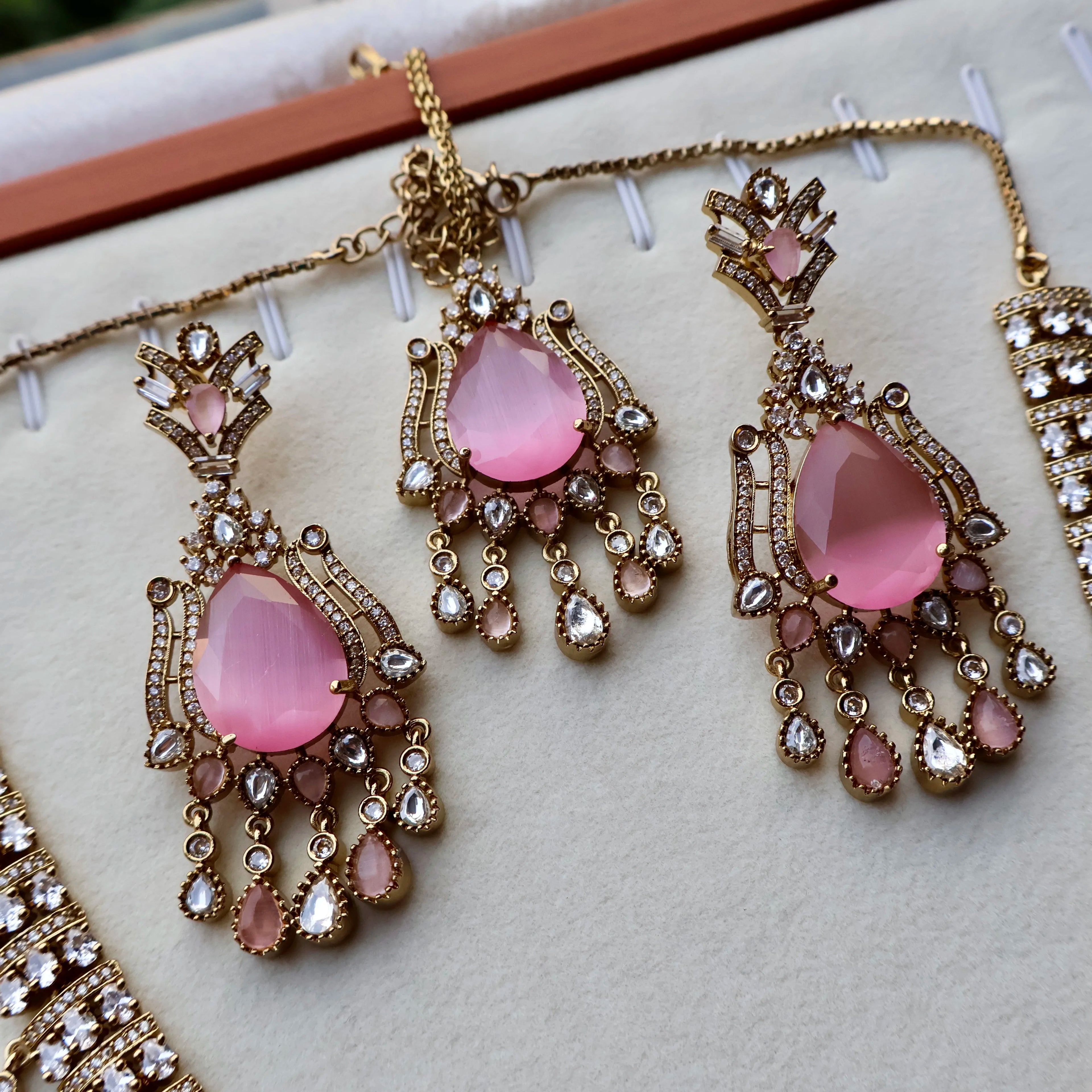 Pink teardrop earrings with gold and crystal details on a white surface