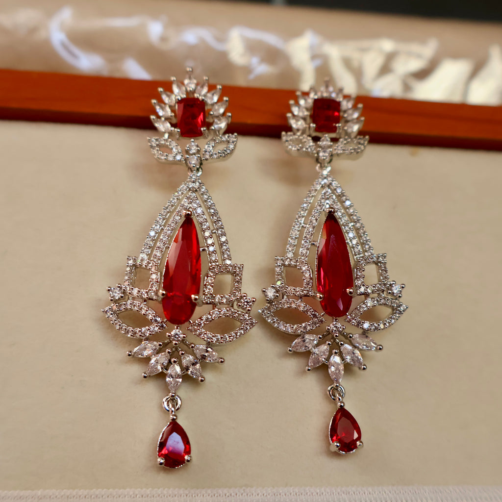 Pair of red gemstone earrings with silver accents on a beige background