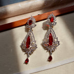 Pair of ornate earrings with red gemstones on a beige surface