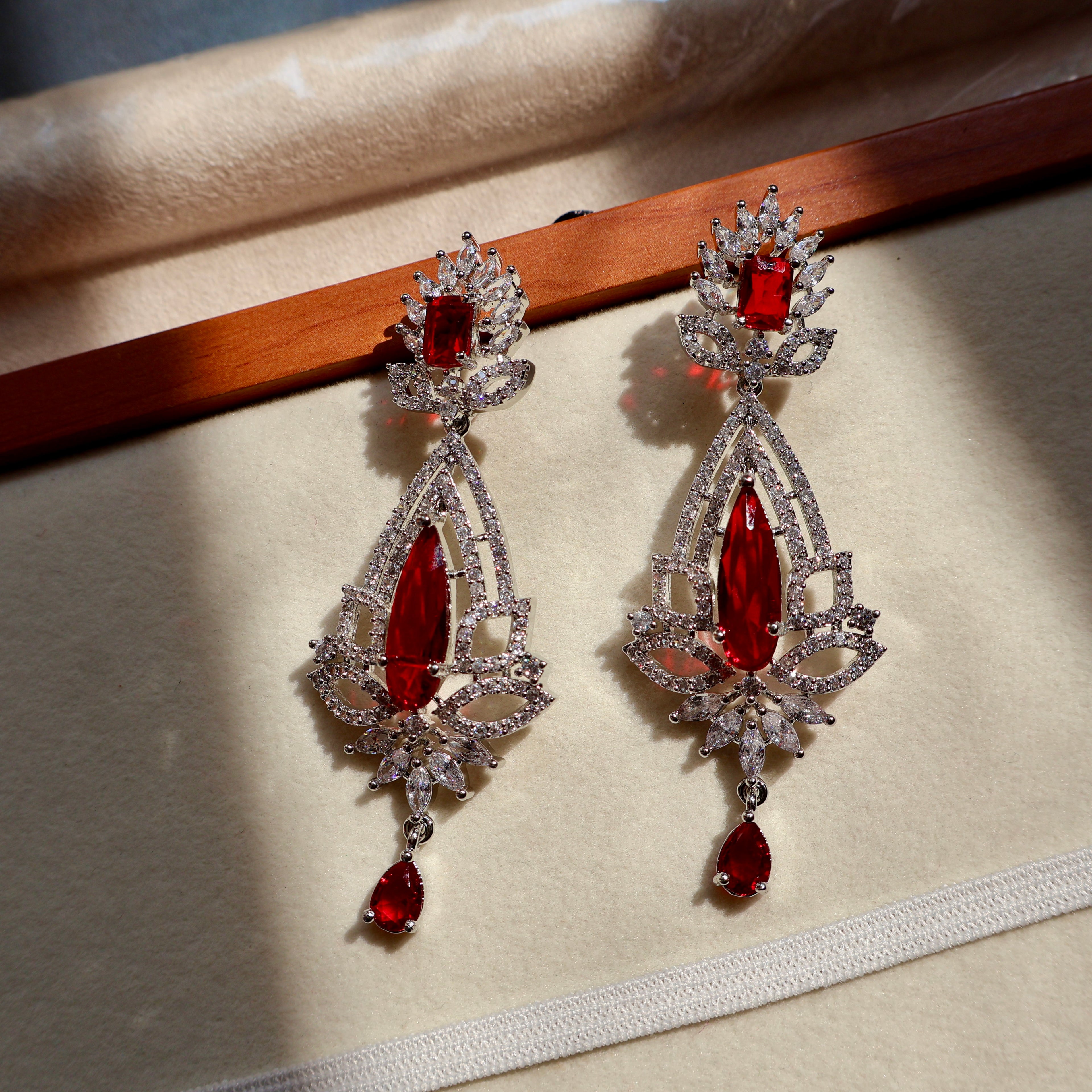 Pair of ornate earrings with red gemstones on a beige surface