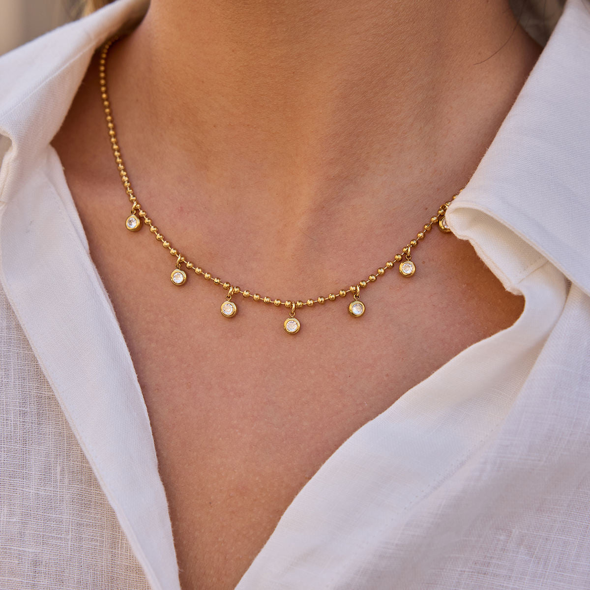 Gold necklace with small round pendants worn by a person in a white shirt.